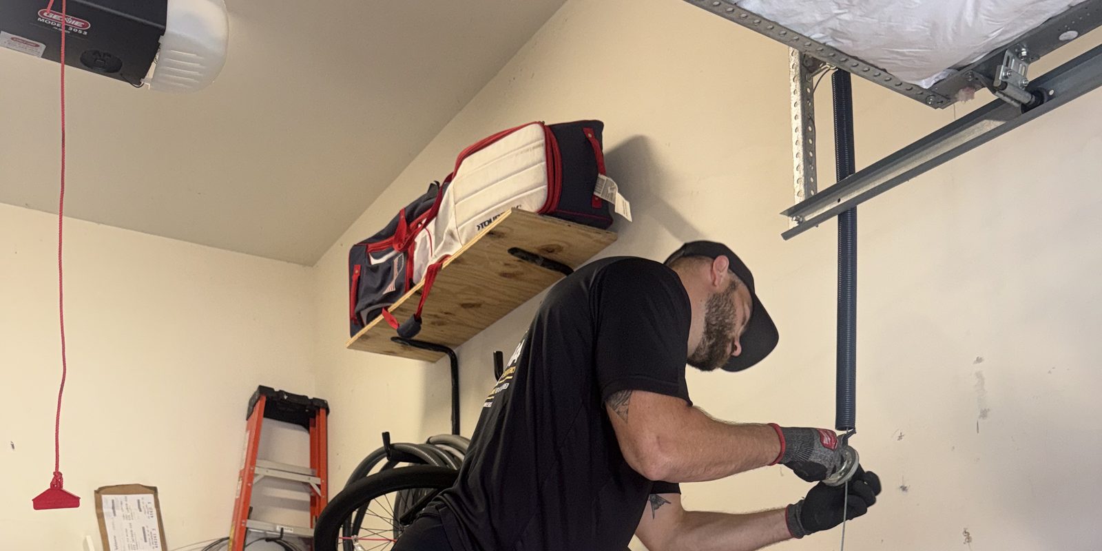 Garage door opener with its red emergency release cord while a Crown technician works on the door