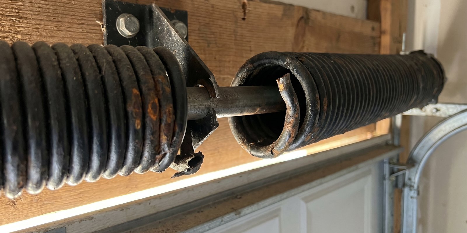 Close-up of worn rusty garage door roller in damaged metal track causing noise
