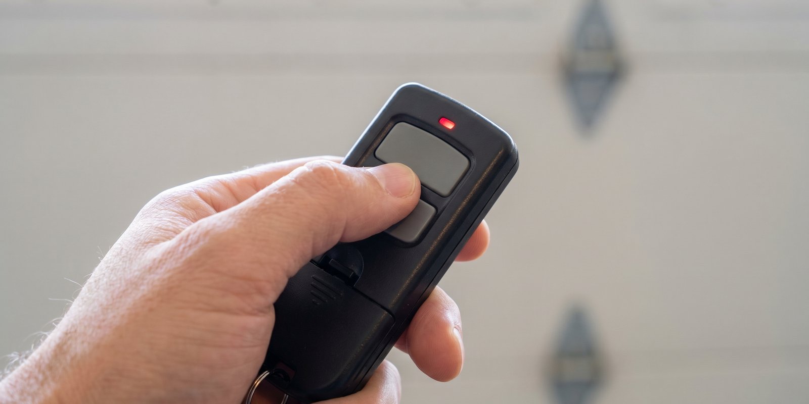 Hand pressing button on black garage door remote control with red LED indicator